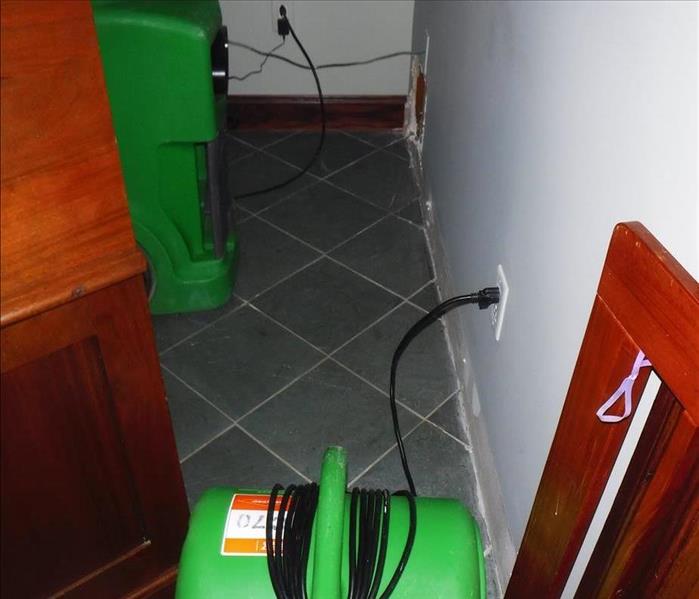 corner of a room with tile floor, baseboard removed and a fan and dehumidifier running