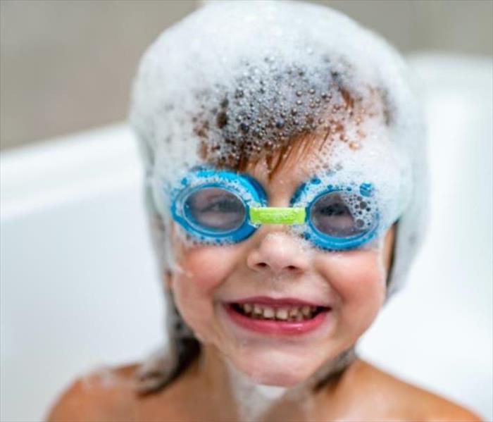 A child in a bathtub with blue goggles on with suds on the child's head