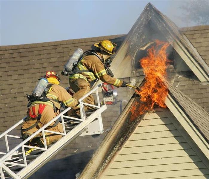 Two firefighters on a ladder trying to put out a fire in a second story window.  